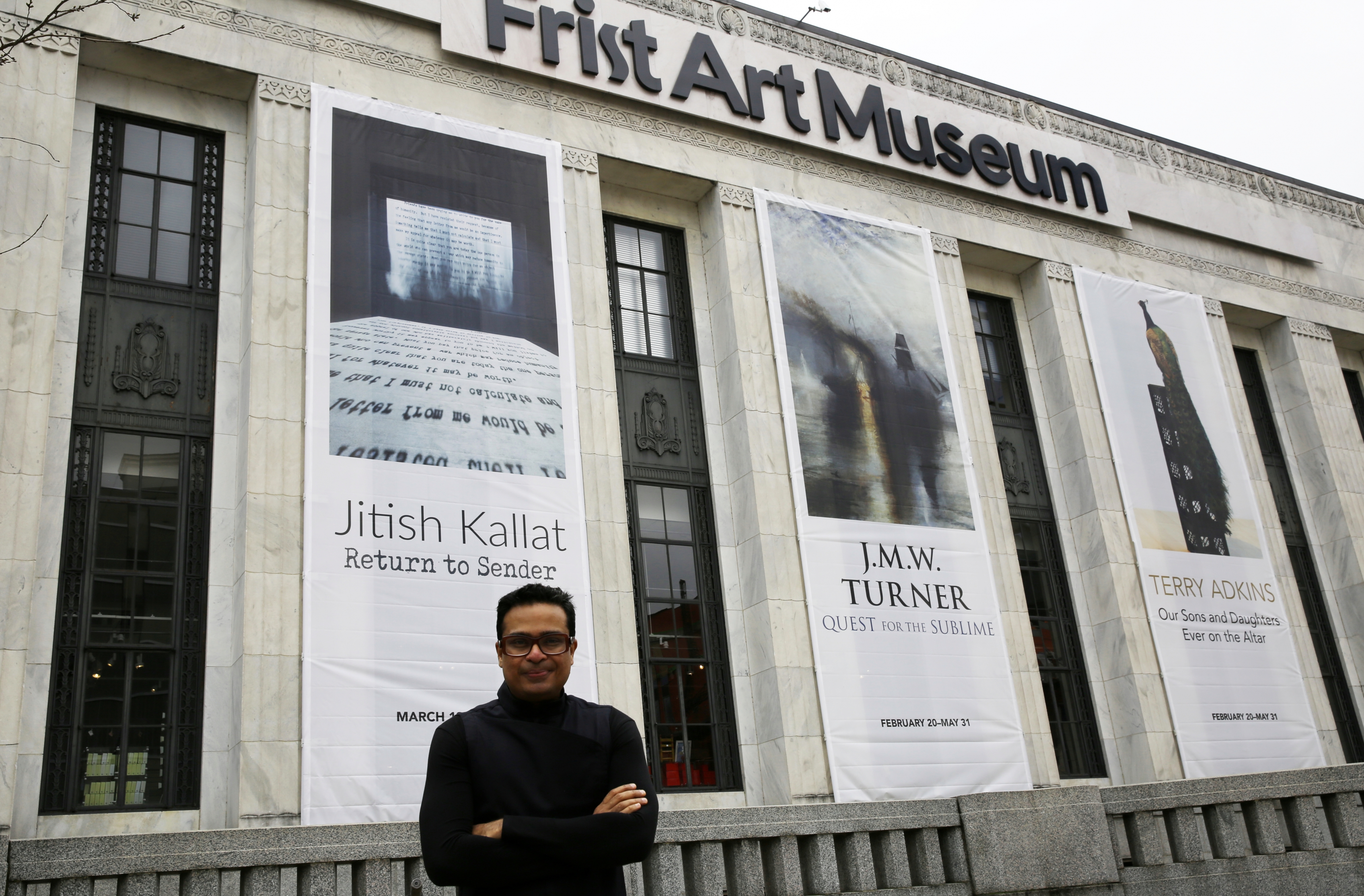 Photo of the artist standing in front of the Frist Art Museum where a banner with his name hangs on the facade